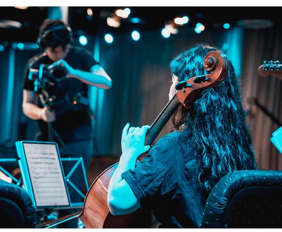 Alumna tocando violoncello en un concierto, con luces de escenario